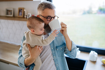 Father holding baby son in arms and drinking coffee.