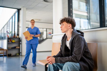 Teenage boy waiting alone in hospital waiting area before medical checkup.