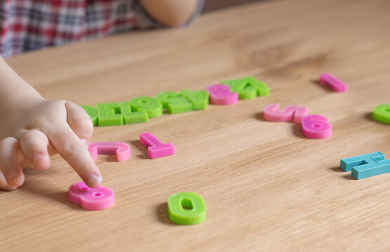 A child learns numbers and letters, hands close-up. Numbers on a wooden table. Preschool education. Homeschooling. Child development at home. Children's hands, fine motor skills