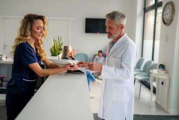 Doctor and nurse discussing important details at the reception desk of a modern hospital clinic, while patients wait in the background, creating a dynamic healthcare environment