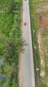Vista a&eacute;rea vertical de carros circulando por uma avenida em meio a uma regi&atilde;o verdejante. A foto destaca o contraste entre a infraestrutura urbana e a natureza ao redor, com o tr&aacute;fego fluindo.