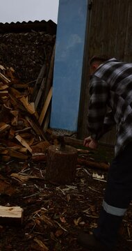 Bearded man in his 30s splitting logs with an axe in a village yard surrounded by wooden houses and nature. erfect for concepts of slow living, traditional work, and seasonal preparation for winter.