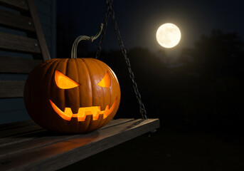 Fototapeta premium Carved Halloween pumpkin on a swing with a full moon in the background, spooky holiday concept.