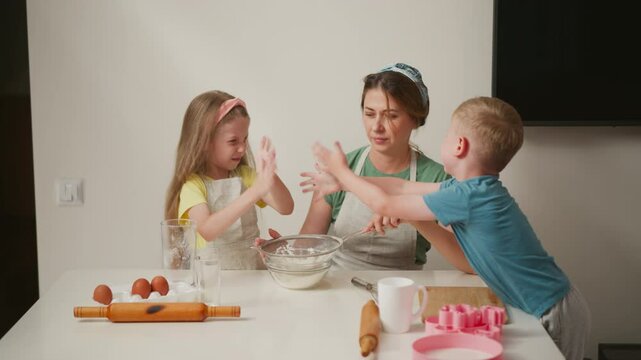 kids playfully dusting flour from hands while baking, causing light mess and laughter as aunt pulls back slightly with surprised expression, showing fun and chaos in family kitchen activity