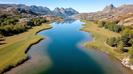 Obraz premium Tranquil Blue River Winding Through Lush Green Valley and Rocky Mountains Under Sunny Sky
