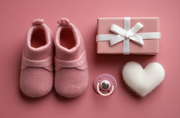 Baby accessories with pacifier, knitted shoes, and gift box on pink background








