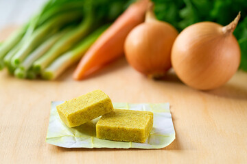 chicken bouillon cubes and fresh vegetables for soup on white wooden table, selective focus.