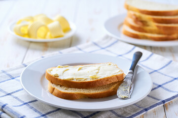 Delicious white wheat bread and fresh butter on a light wooden table, selective focus.