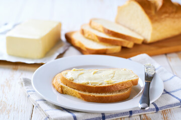 spreading butter in to white wheat bread slices on a light kitchen table.