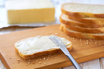 Tasty cut wheat bread  with fresh butter on a white wooden table.