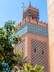 Historic Kasbah Mosque, also known as Moulay al-Yazid Mosque, in Marrakech, Morocco, beautiful Islamic architecture with detailed geometric patterns, blue mosaic tiles and palm trees under spring sky.