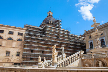 Historic Piazza Pretoria in Palermo, Sicily, featuring the famous Fountain of Shame and a dome under restoration, with scaffolding against a bright blue sky and elegant marble statues in foreground
