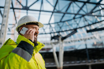 Construction site manager making phone call while inspecting building site.