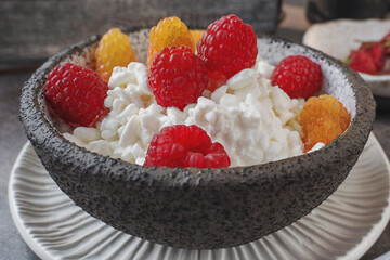 Creamed cottage cheese with raspberries. An easy healthy breakfast. A bowl filled with grainy, creamy cottage cheese is garnished with bright yellow and red raspberries. Close-up.