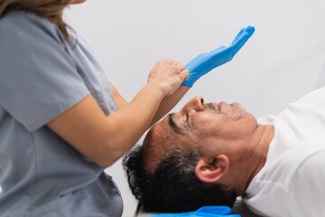 Fototapeta premium Physiotherapist putting on protective gloves while assisting a senior patient lying on a bed in a medical clinic