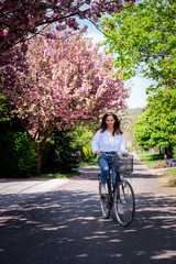 Happy woman in fashionable clothes riding bicycle on suburban neighborhood street in spring
