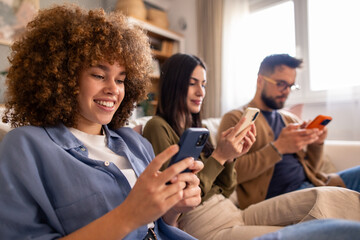 Multiethnic Group Of Young Adults Browsing Social Media On Phones While Relaxing On Comfortable Couch