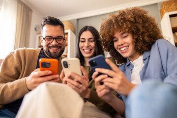 Smiling Diverse Friends Sitting on Couch Sharing Laughter and Enjoying Smartphones Together
