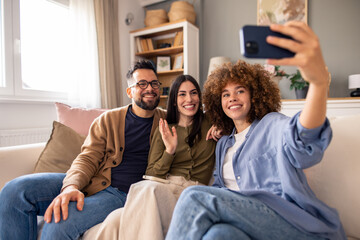 Three Friends Smiling on a Couch Taking a Selfie in a Cozy and Bright Living Room