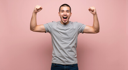 Fototapeta premium Enthusiastic young man with short hair raising fists in victory pose on pink background. Joyful facial expression. Achievement. Motivational, personal success stories, fitness, positive psychology