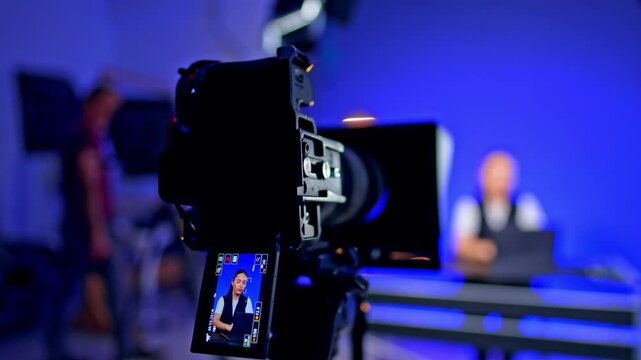 Brunette girl on the camera display. Blog recording. Man walks at blurred backdrop behind the stages.