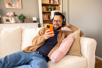 Relaxed Man Wearing Headphones Smiling at Phone While Lounging on a Cozy Indoor Couch