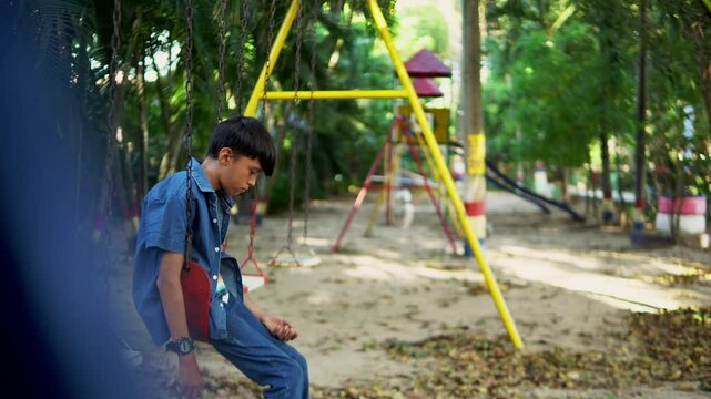 Sad child sitting alone on a swing in a playground