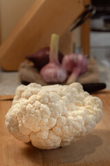 Whole head of cauliflower lies on a kitchen cutting board. Close-up