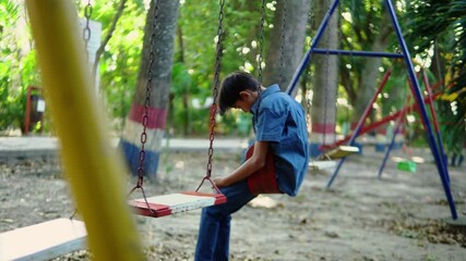 Pensive latin boy sitting on a swing looking down