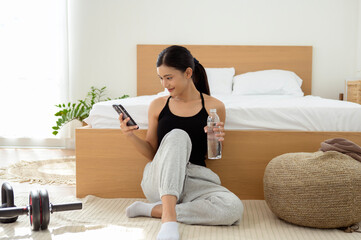  young Asian sporty woman using smartphone after workout in living room