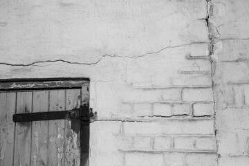 Old wooden door hanging on rusted hinges with a damaged wall