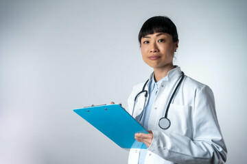 Happy smiling asian female doctor writing on clipboard, isolated on background. Medicine and health...