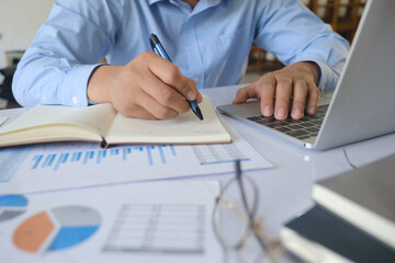 Businessman writing notes while working on laptop during financial data analysis