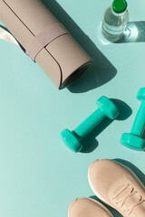 Sport or workout concept flat lay with blue dumbbells, sneakers, yoga mat on the blue teal background. Copy space