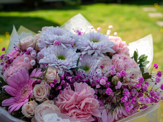 Beautiful bouquet with pink roses, pink carnations, pink gerberas, white chrysanthemums, and pink baby's breath on a garden background.