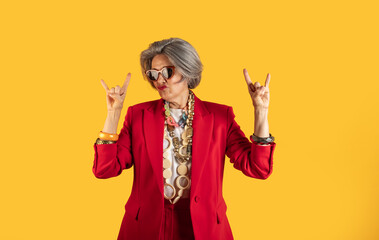 Senior businesswoman making rock and roll hand gesture on yellow background