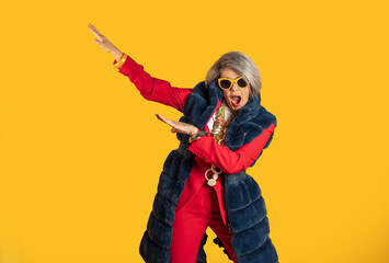 Stylish senior woman dancing and having fun on yellow background