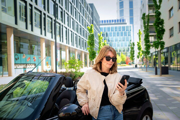 Mid aged woman standing next to her car and using her smartphone