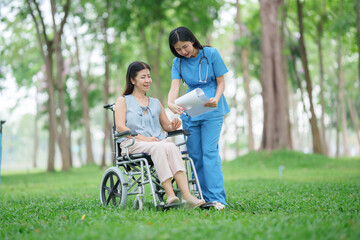 Fototapeta premium Asian elderly care nurse talking to elderly female patient in wheelchair outdoors at park. Asian doctor, helping and supporting the elderly, rehabilitation and health care.