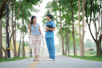 Obraz premium Elderly white woman sitting in wheelchair with young Asian nurse in green grass park
