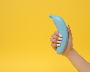 Unusual concept with blue banana held by female hand on colorful background..Trendy pop-art photo...