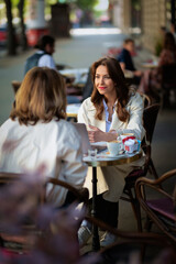 Two female friends sitting at outdoor cafe in the city and talking