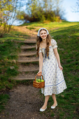 Fine art portrait of a young woman wearing light dress walking in a summer field with a basket of...
