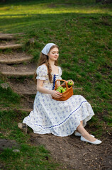 Fine art portrait of a young woman wearing light dress walking in a summer field with a basket of...