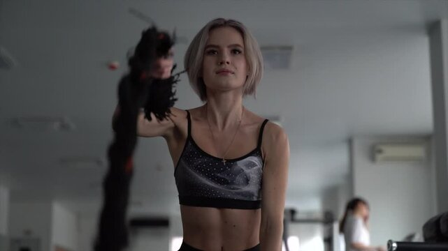 sstkWellness , Athletic girl focused on fitness training with ropes at gym, Sport. Attractive young fit sportswoman working out in functional training gym doing exercise with battle ropes.