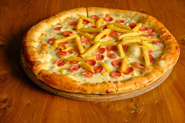 Pizza with French fries and sausage slices on a wooden table.