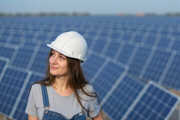 Focused Female Technician in Hard Hat and Overalls Observing Solar Farm, Extensive Panel Field, Side View.