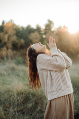 Young woman praying with hands joined at sunset in nature expressing gratitude and hope