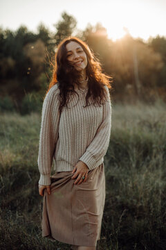 Young woman wearing sweater and skirt enjoying golden hour sunlight in meadow