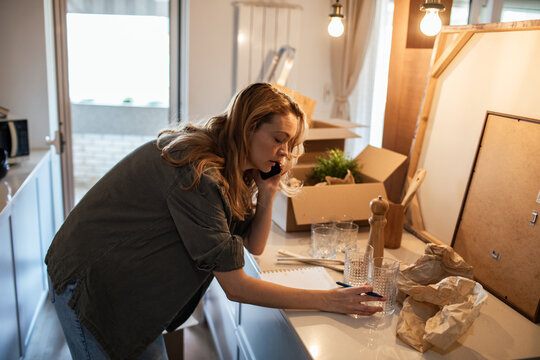 Woman talking on smartphone while unpacking boxes in new kitchen